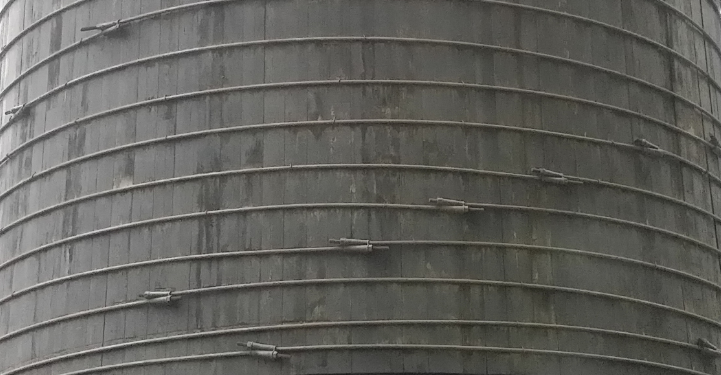 Close-up of a weathered cylindrical concrete structure with metal support rods, gray tones, industrial mood